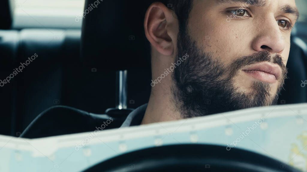 Young bearded man holding map while sitting in car