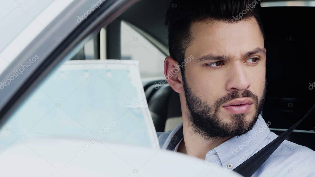 Young bearded man looking away while sitting in car with map