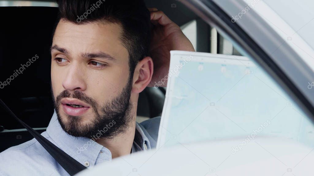 Young man touching head and thinking while sitting in car with map