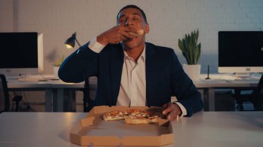Afrika kökenli Amerikalı işadamı gece ofiste paket pizza yiyor. 
