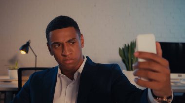 Kızgın Afrikalı Amerikalı iş adamı, akşam saatlerinde akıllı telefondan selfie çekiyor. 
