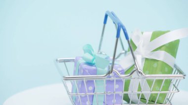 Mavi arka planda paketlenmiş hediye kutularıyla alışveriş sepeti.