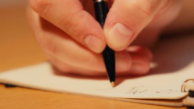 close up view of man holding pen while writing on notebook  clipart