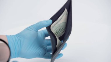 Beyaz arka planda dolar banknotlu cüzdan gösteren lateks eldivenli kişi görüntüsü. 