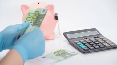 cropped view of person in latex gloves counting euro banknotes near calculator and piggy bank on white background  clipart