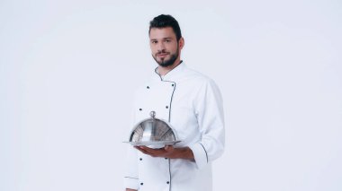 Servis tabağı ve saati olan genç aşçı beyaz kameraya bakıyor.