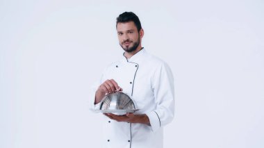brunette man in chef jacket holding serving dish with cloche and looking at camera isolated on white clipart