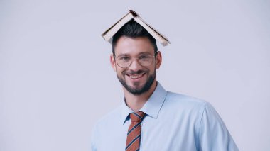 Kafası hakkında kitabı olan neşeli öğretmen gri kameraya gülümsüyor.