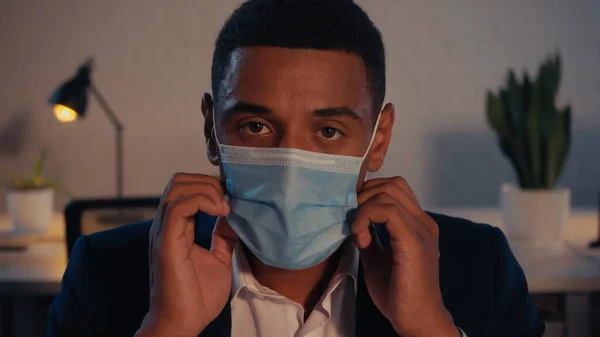 African american businessman in medical mask looking at camera in office at night