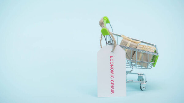small shopping cart with gifts and card with economic crisis lettering on blue background 