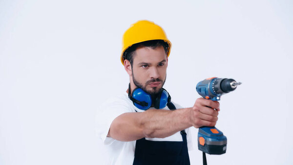 серьезный мастер в защитном шлеме, работающий с электрической дрелью, изолированной на белом