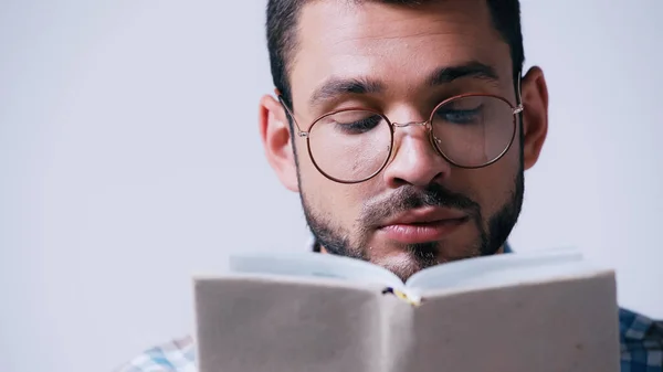 focused student in eyeglasses reading blurred book isolated on grey