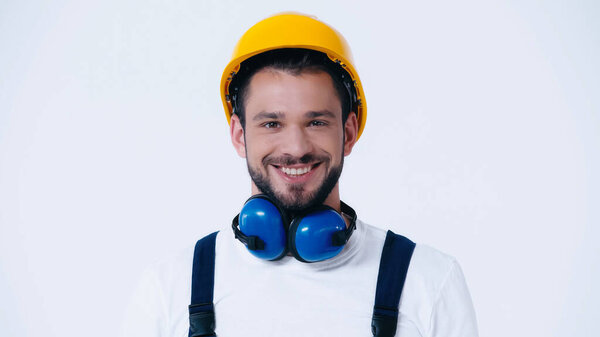 веселый строитель с шумом отмены наушники и каска глядя на камеру изолированы на белом