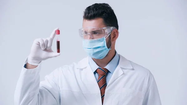 virologist in goggles and medical mask holding blood sample in test tube isolated on grey