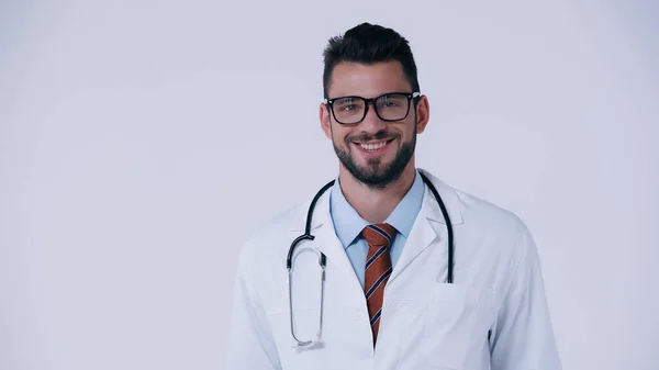 身穿白衣和眼镜的快乐的年轻医生对着用灰色隔离的相机微笑 — 图库照片