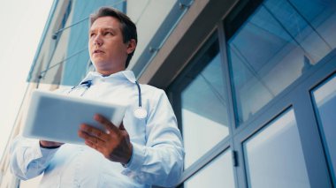 Klinik binasının yakınında dijital tabletli doktorun düşük açılı görüntüsü
