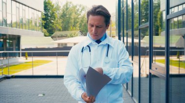Steteskoplu bir doktor, dışarıda dokümanların olduğu klasörü tutuyor.