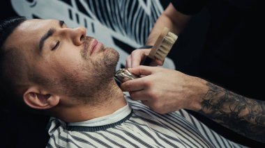 Kuaförde saç fırçası tutan ve müşterinin sakalını kesen dövmeli berber. 