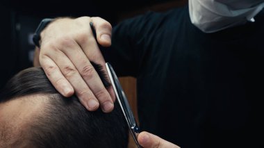 Tıbbi maskeli kuaför, berber dükkanında saç kesiyor. 