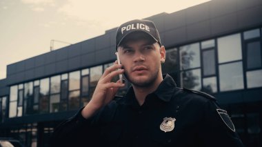 Üniformalı ve rozetli ciddi bir polis şehir caddesinde akıllı telefondan konuşuyor.  