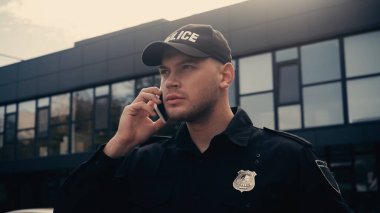 Üniformalı ve rozetli bir polis şehir caddesinde akıllı telefondan konuşuyor.  