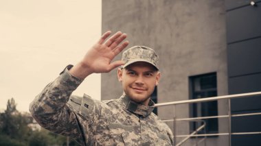 Dışarıda yürürken üniformalı ve şapkalı gülümseyen asker. 