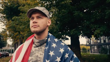 Amerikan bayrağı taşıyan gururlu asker dışarıda askeri üniforma içinde duruyor. 
