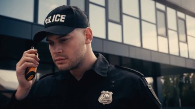 Üniformalı ve şapkalı genç bir polis dışarıda telsiz kullanıyor. 