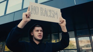 Kapüşonlu genç adam dışarıda ırkçılık yazmayan bir pankart tutuyor. 