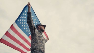 Üniformalı ve şapkalı Amerikan bayrağını açık havada tutan askerin alçak açılı görüntüsü 
