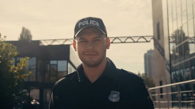 Şapkalı ve üniformalı neşeli polis memuru şehir sokağındaki kameraya bakıyor.