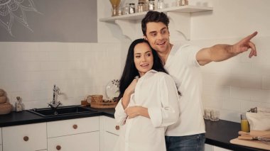 Sevgilisini kucaklayan mutlu bir adam ve mutfaktaki parmağıyla işaret ediyor.