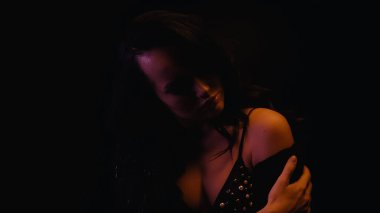 Sütyen giymiş, koluna dokunan seksi bir kadın, siyah ışıkla izole edilmiş. 