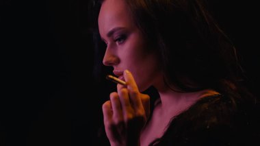 Genç bir kadın sigarasını tutuyor ve siyah üzerine bakıyor. 