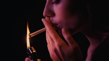 Siyah üzerine izole edilmiş sigara ve çakmak tutan genç bir kadın. 