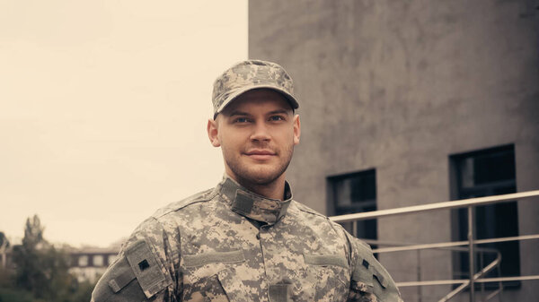Smiling soldier in uniform and cap looking away while walking outdoors 