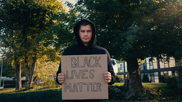young activist in hoodie holding placard with black lives matter lettering outside