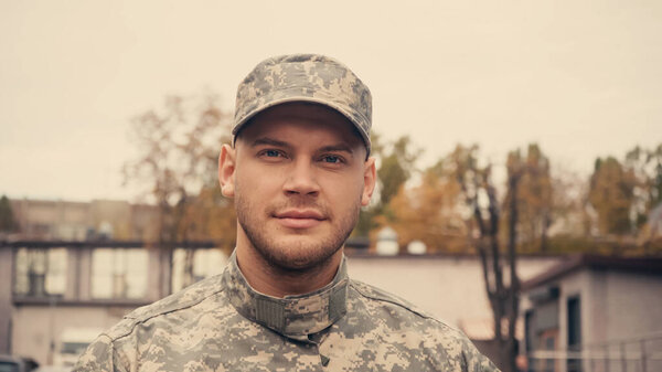 portrait of young soldier in uniform and cap looking at camera outdoors 