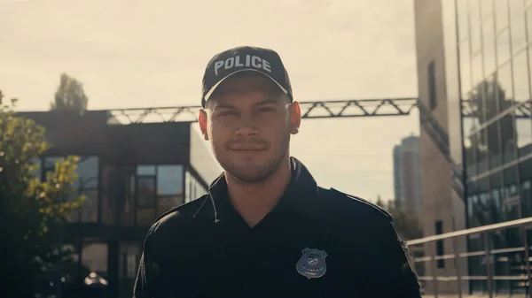 头戴便帽 身穿警服的快乐的警察看着城市街道上的摄像头 — 图库照片