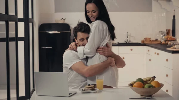 Σέξι Γυναίκα Αγκαλιάζει Ευτυχισμένο Άνδρα Κοντά Στο Πρωινό Και Laptop — Φωτογραφία Αρχείου