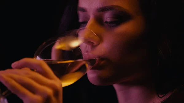 年轻女子喝着用黑色玻璃杯隔开的白葡萄酒 — 图库照片