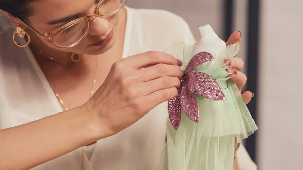 Seamstress in eyeglasses making dress on small mannequin in workshop