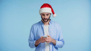 Kırmızı Noel Baba şapkalı sakallı adam mavi telefondan mesaj yolluyor. 