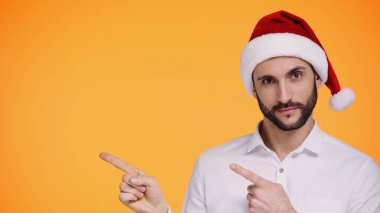 Kırmızı Noel Baba şapkalı sakallı adam sarıyı gösteren parmaklarıyla işaret ediyor. 