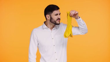 displeased man in white shirt holding stinky socks isolated on yellow  clipart