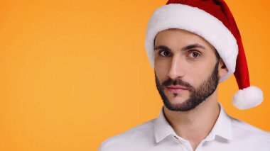 Kırmızı Noel Baba şapkalı sakallı adamın portresi. Sarı renkli kameraya bakıyor.