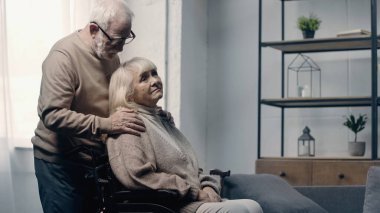 Kıdemli adam tekerlekli sandalyede bunamış karısını sakinleştiriyor. 