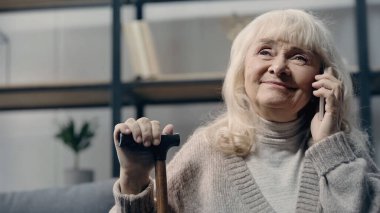 Akıllı telefondan konuşan ve bastonu tutan son sınıf öğrencisi mutlu bir kadın. 