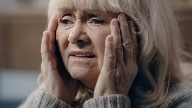 Senior woman with dementia suffering from headache and touching head clipart