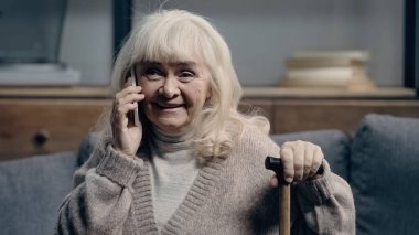 Elinde bastonla cep telefonuyla konuşan neşeli, son sınıf öğrencisi bir kadın.